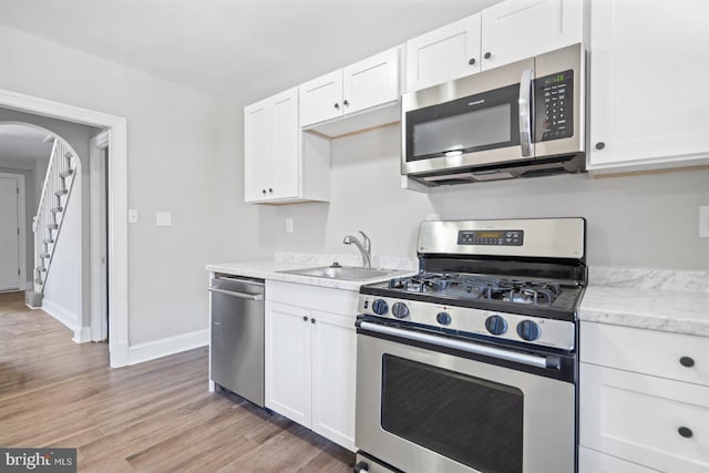 kitchen featuring arched walkways, a sink, white cabinets, light wood-style floors, and appliances with stainless steel finishes