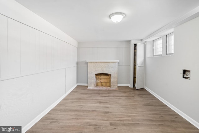 unfurnished living room with a brick fireplace, wood finished floors, and baseboards