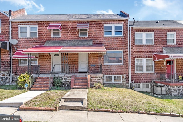 view of property featuring central air condition unit, brick siding, and a front yard