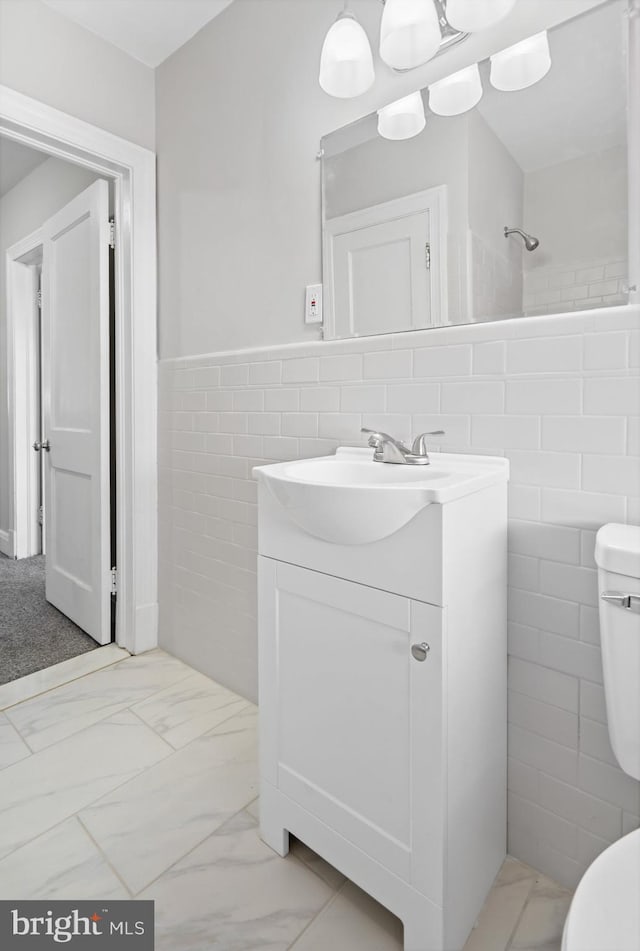 bathroom featuring tile walls, toilet, wainscoting, marble finish floor, and vanity