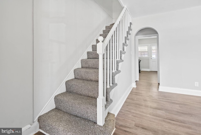 stairs featuring wood finished floors, arched walkways, and baseboards