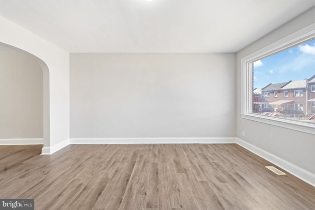 unfurnished room with visible vents, arched walkways, baseboards, and wood finished floors