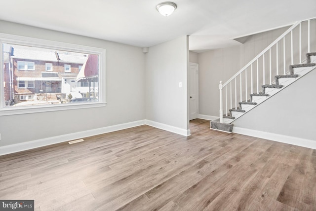 spare room with stairway, visible vents, baseboards, and wood finished floors