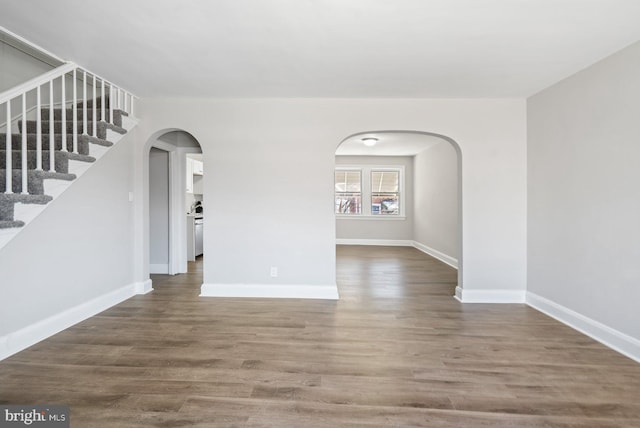 spare room featuring arched walkways, stairway, baseboards, and wood finished floors