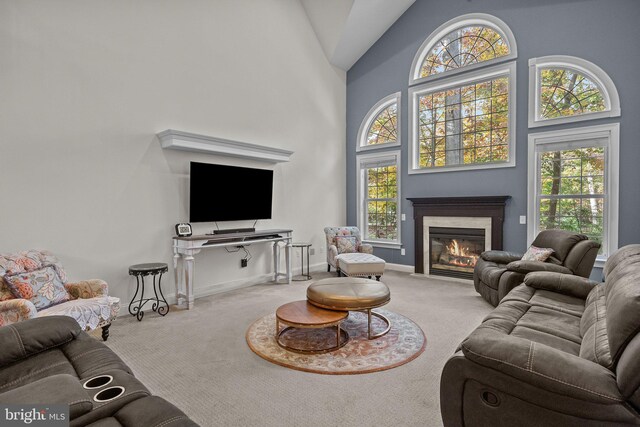 carpeted living area featuring a wealth of natural light, baseboards, a fireplace with flush hearth, and high vaulted ceiling