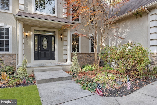 property entrance with stone siding, roof with shingles, and stucco siding