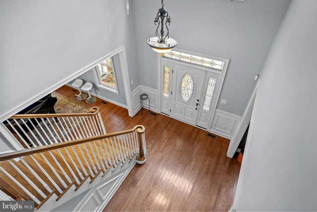 foyer with wood finished floors, visible vents, a wainscoted wall, a high ceiling, and a decorative wall