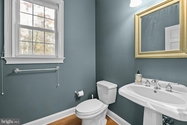 half bathroom with wood finished floors, toilet, baseboards, and a sink