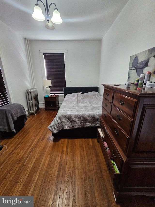 bedroom with an inviting chandelier, dark wood-style floors, and radiator heating unit