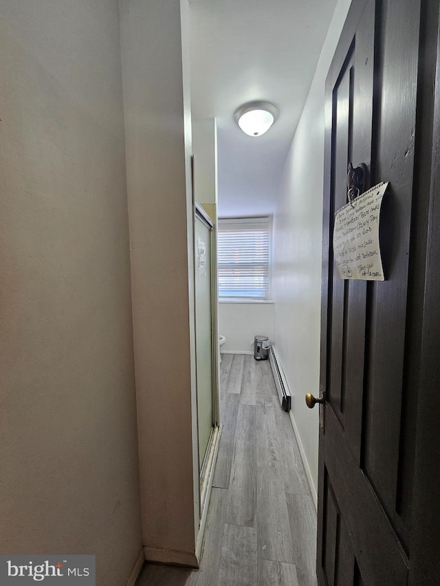 corridor featuring light wood finished floors, a baseboard heating unit, and baseboards