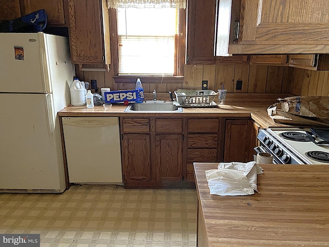 kitchen with wooden walls, light floors, butcher block counters, white appliances, and a sink