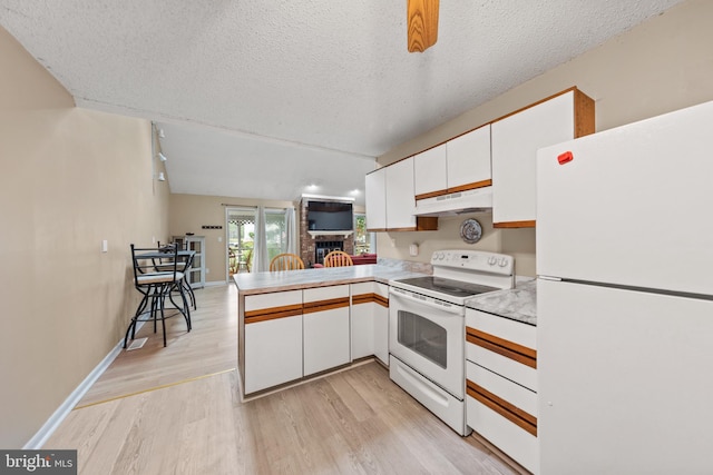 kitchen with under cabinet range hood, white appliances, light wood-style floors, a peninsula, and white cabinets