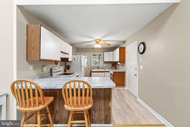 kitchen with white appliances, a peninsula, light countertops, a textured ceiling, and light wood-type flooring