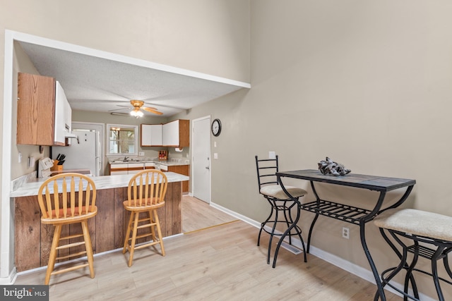 kitchen with light wood finished floors, light countertops, a kitchen bar, a peninsula, and stove