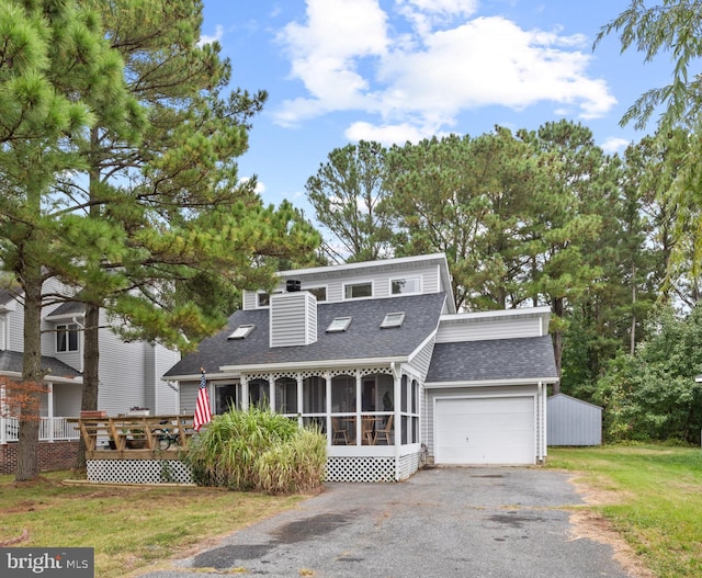 view of front of home with a shingled roof, a front lawn, aphalt driveway, a garage, and a sunroom