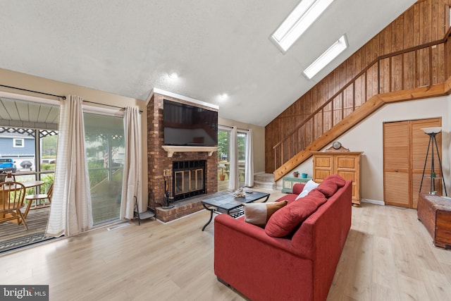 living room with light wood-type flooring, high vaulted ceiling, a skylight, a fireplace, and stairs