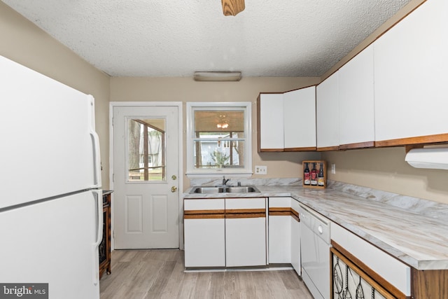 kitchen featuring white appliances, light wood finished floors, a sink, light countertops, and white cabinetry