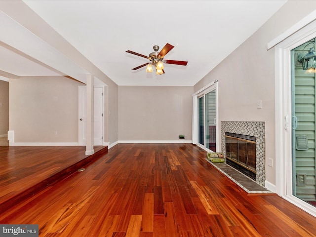 unfurnished living room with ceiling fan, a fireplace, baseboards, and wood finished floors