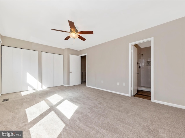 unfurnished bedroom featuring baseboards, visible vents, carpet floors, and multiple closets