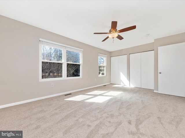 unfurnished bedroom with light carpet, baseboards, and multiple closets