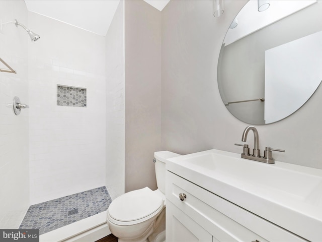 full bathroom featuring tiled shower, toilet, and vanity