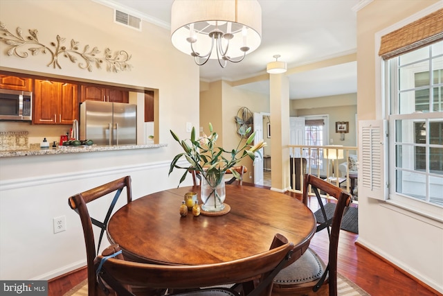 dining space with visible vents, wood finished floors, ornamental molding, and a chandelier