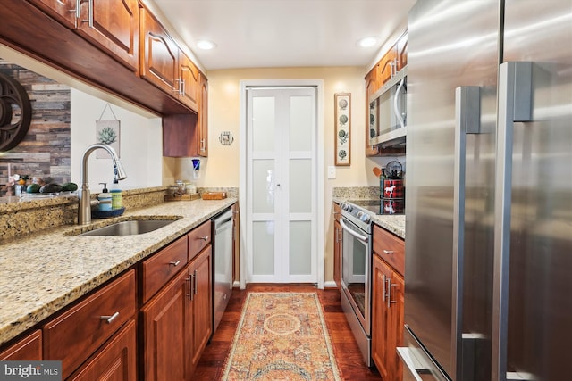 kitchen featuring dark wood finished floors, light stone countertops, appliances with stainless steel finishes, and a sink