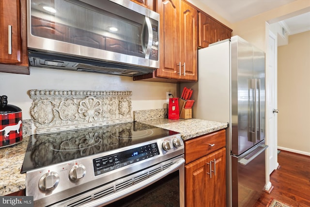 kitchen featuring ornamental molding, light stone counters, brown cabinets, stainless steel appliances, and dark wood-style flooring