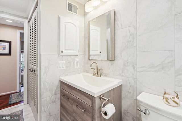 half bath with visible vents, toilet, ornamental molding, marble finish floor, and vanity