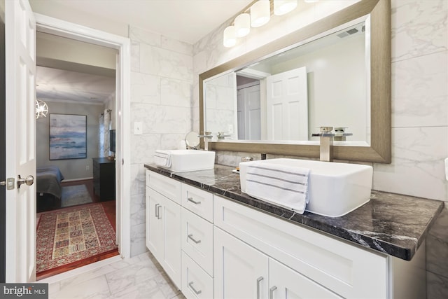 ensuite bathroom with tile walls, double vanity, marble finish floor, and a sink