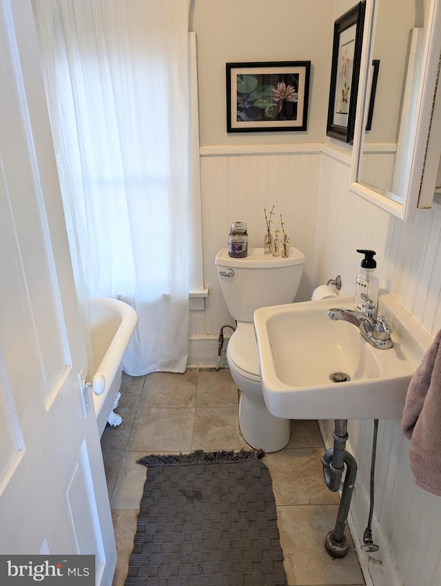 bathroom featuring wainscoting, toilet, a tub to relax in, and a sink