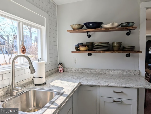 kitchen featuring open shelves, backsplash, and a sink