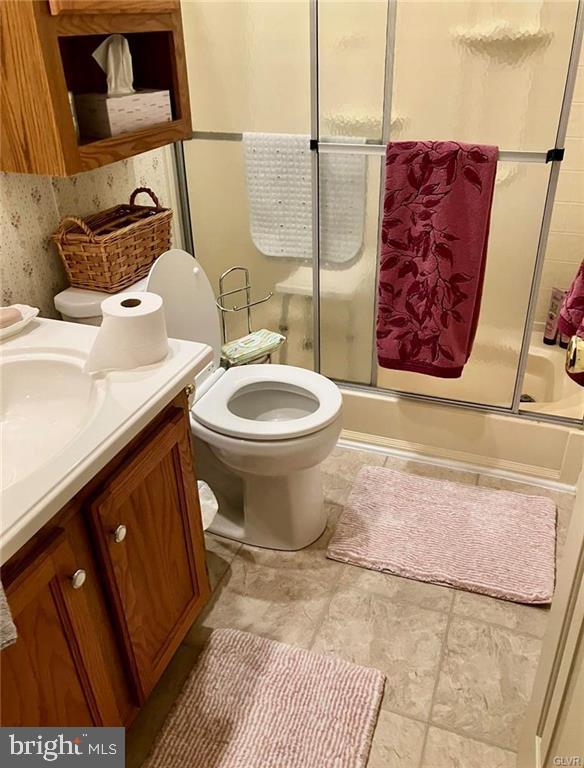 bathroom with enclosed tub / shower combo, toilet, and vanity