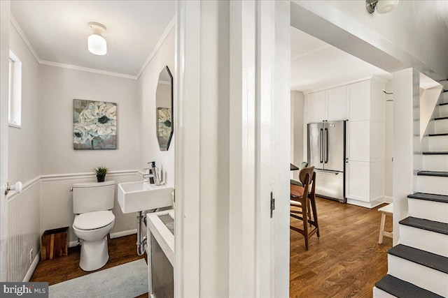 bathroom featuring toilet, ornamental molding, a sink, wood finished floors, and baseboards