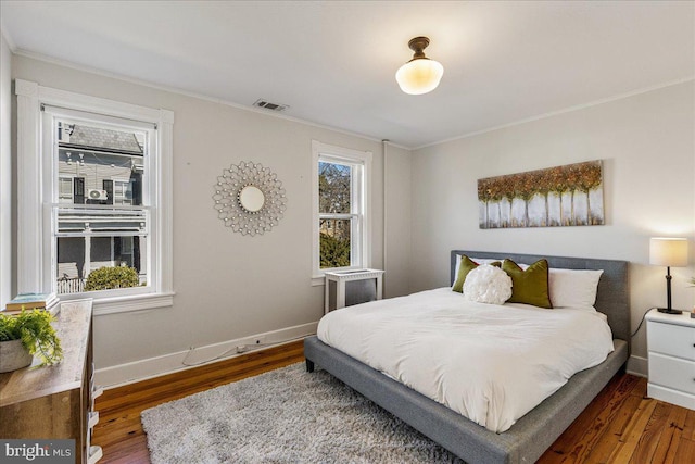 bedroom with visible vents, ornamental molding, baseboards, and wood finished floors