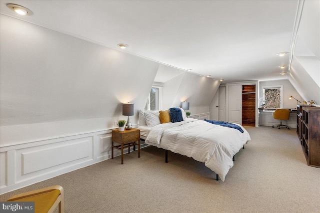 bedroom featuring light colored carpet, lofted ceiling, wainscoting, a closet, and a decorative wall