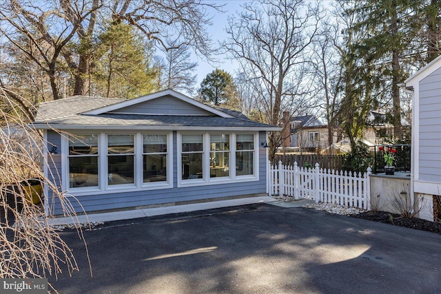 exterior space featuring aphalt driveway, fence, and roof with shingles