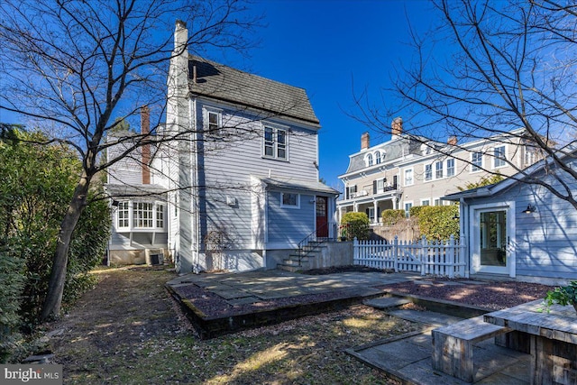 rear view of property featuring entry steps, fence, central AC unit, a chimney, and a patio area