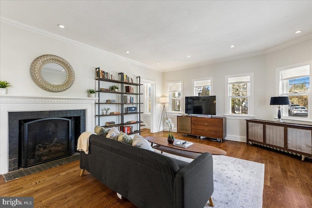 living room featuring a fireplace with flush hearth, recessed lighting, crown molding, and wood finished floors