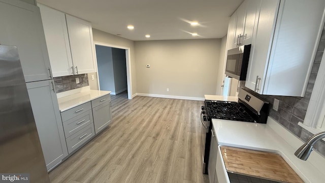 kitchen featuring light wood-type flooring, gray cabinetry, stainless steel appliances, light countertops, and baseboards