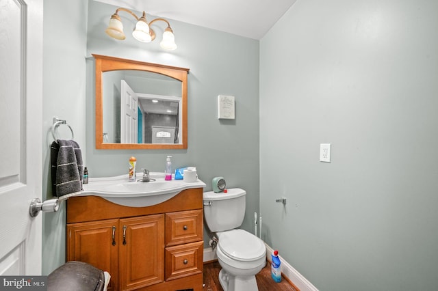 half bath with baseboards, toilet, wood finished floors, and vanity