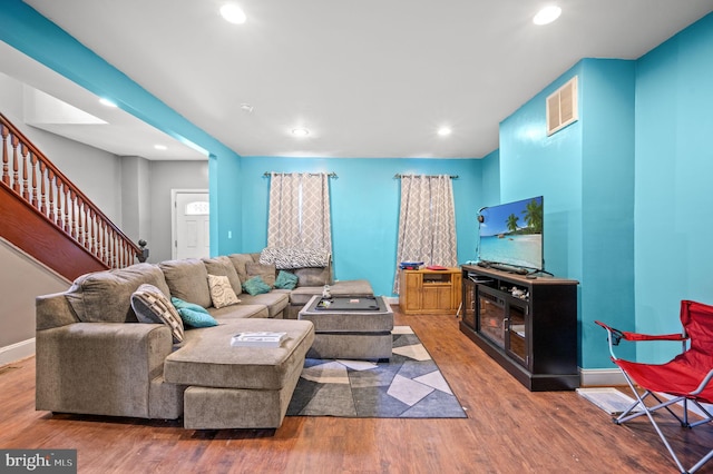 living room with visible vents, baseboards, wood finished floors, and stairs