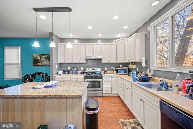 kitchen featuring light wood finished floors, a kitchen island, a sink, under cabinet range hood, and appliances with stainless steel finishes