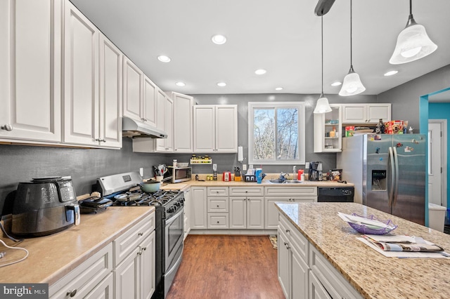 kitchen with under cabinet range hood, stainless steel appliances, white cabinets, and a sink