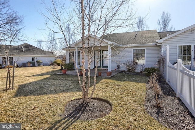 view of front facade featuring a shingled roof, a front lawn, a patio, and fence