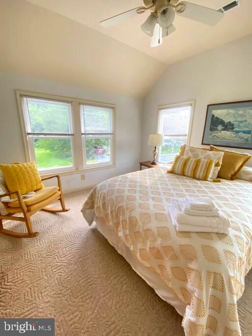 carpeted bedroom featuring visible vents, lofted ceiling, and ceiling fan