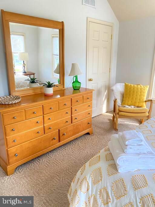 carpeted bedroom featuring vaulted ceiling and visible vents