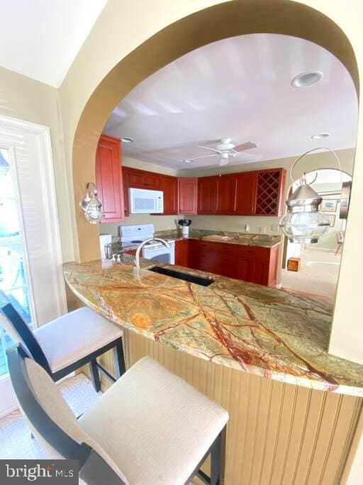 kitchen with a ceiling fan, white appliances, arched walkways, a peninsula, and dark brown cabinets