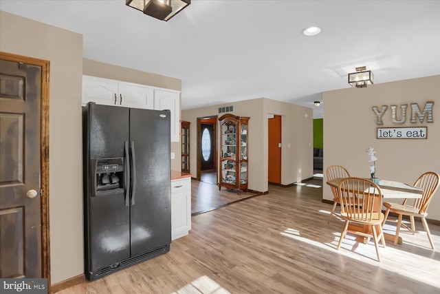 kitchen featuring visible vents, baseboards, light wood-type flooring, black fridge, and white cabinets