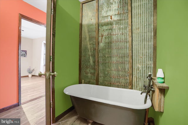 bathroom with a freestanding tub, baseboards, and wood finished floors